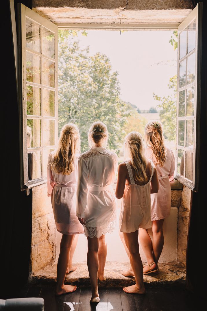 Bridal party looking out the window at a destination wedding in matching satin bridesmaid robes