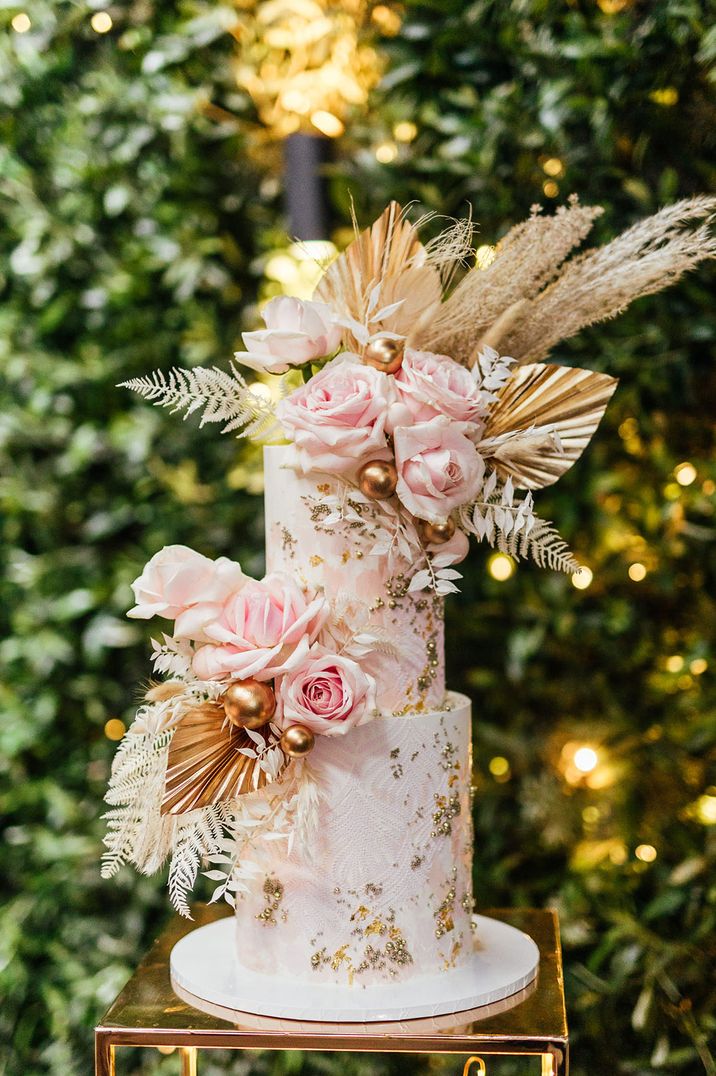 Two tier wedding cake with dried palm leaves, gold gilt and pink flower decor 