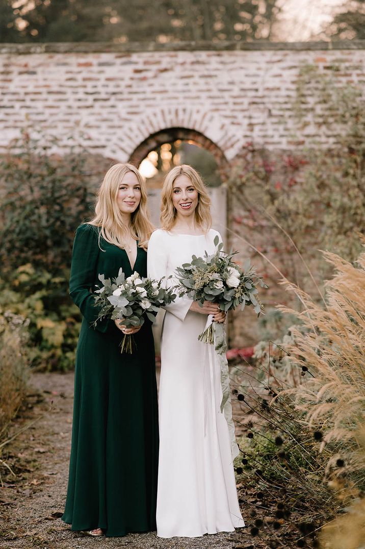 Bridesmaid in emerald green v-neck bridesmaid dress with bride in boat neck long sleeve wedding dress 