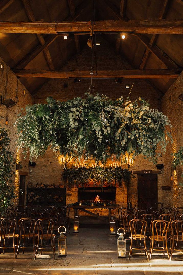 Wedding reception room at Cripps Barn wedding venue with large green foliage hanging decoration and wooden chairs