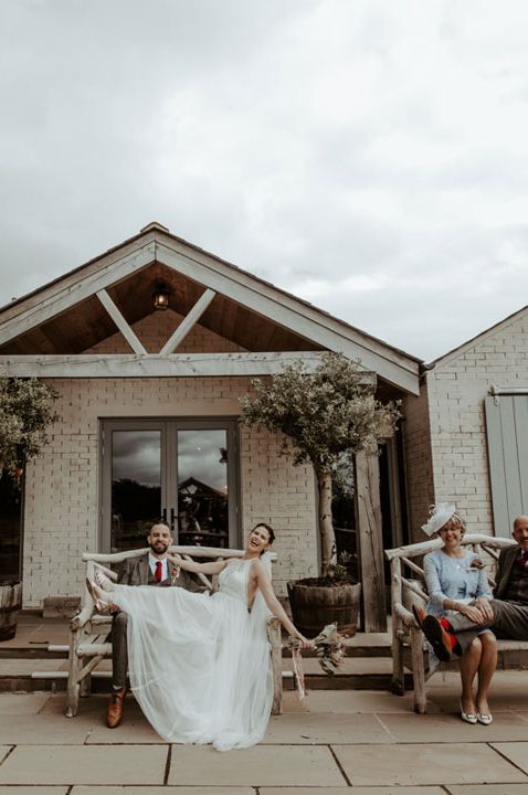 Wedding party sitting and standing on wooden benches outside Eden Barn wedding venue