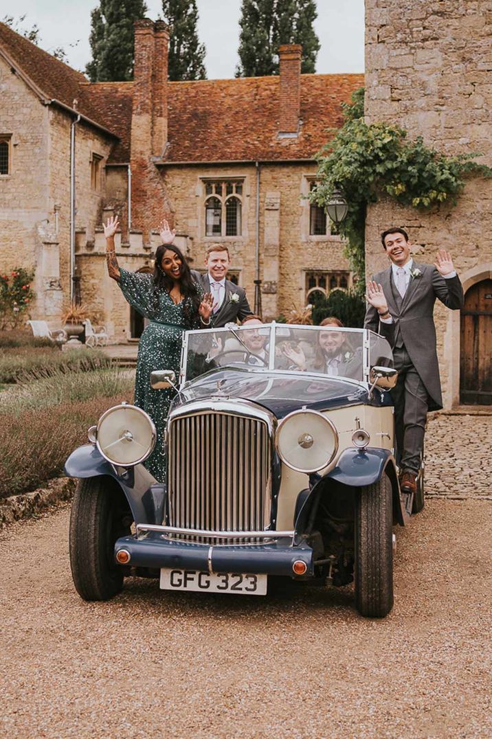 Mixed gender wedding party in old vintage wedding car with groomswoman in bottle green sparkly dress