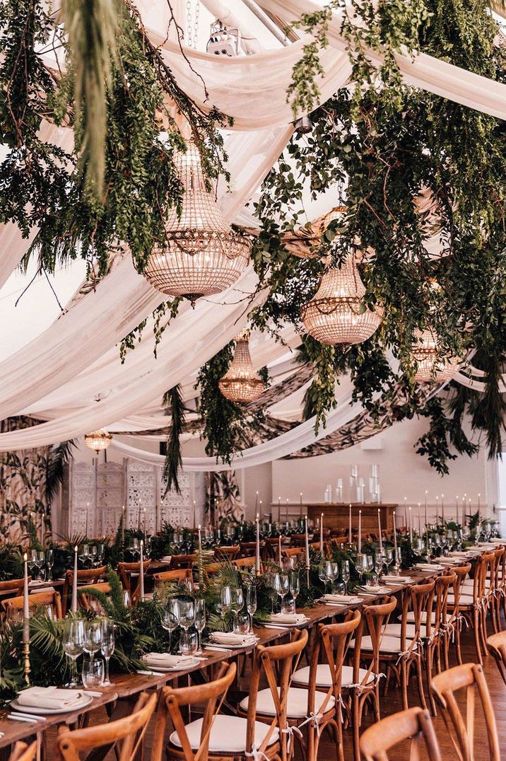 Greenery themed wedding tablescape with suspended foliage, diamond chandeliers, tapered candles, wedding drapes and foliage table centrepieces 