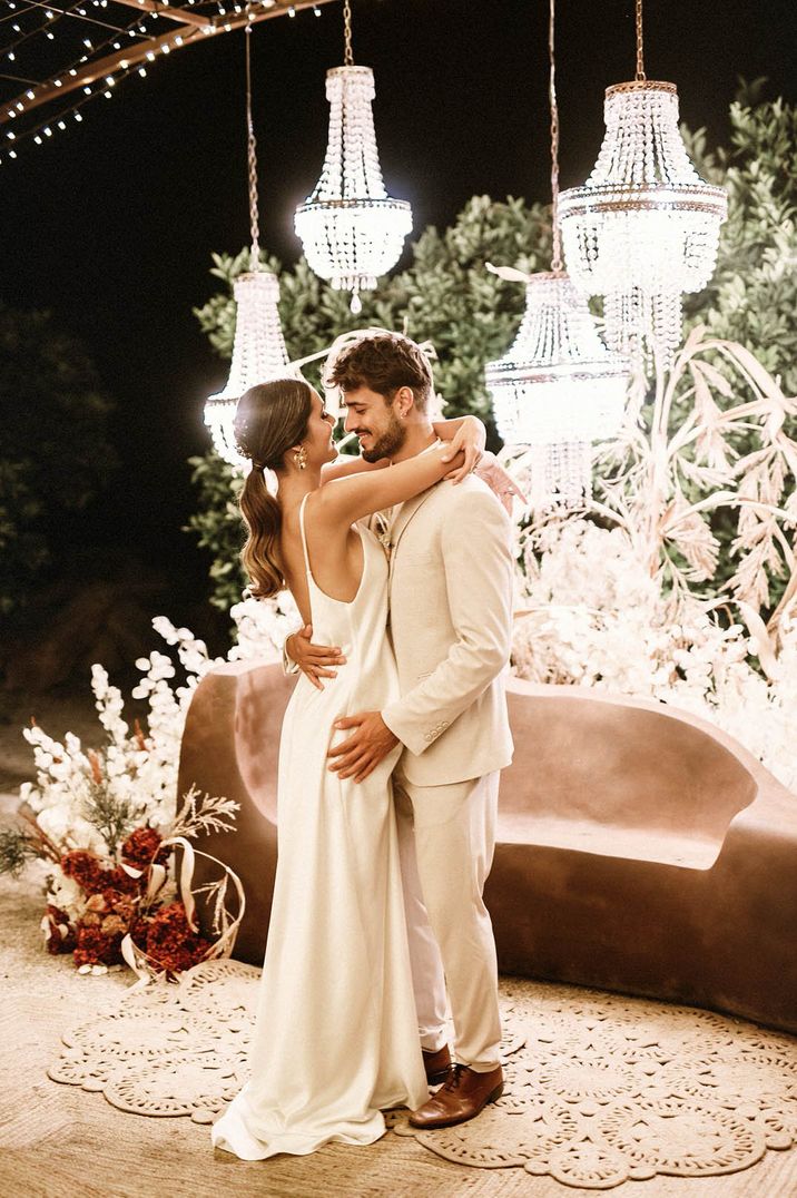 Boho destination wedding with the bride in a simple and elegant satin open back wedding dress embracing the groom 