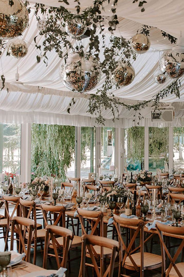 Sparkling disco balls hanging from the marquee at the farm wedding venue with foliage and pink taper candles 