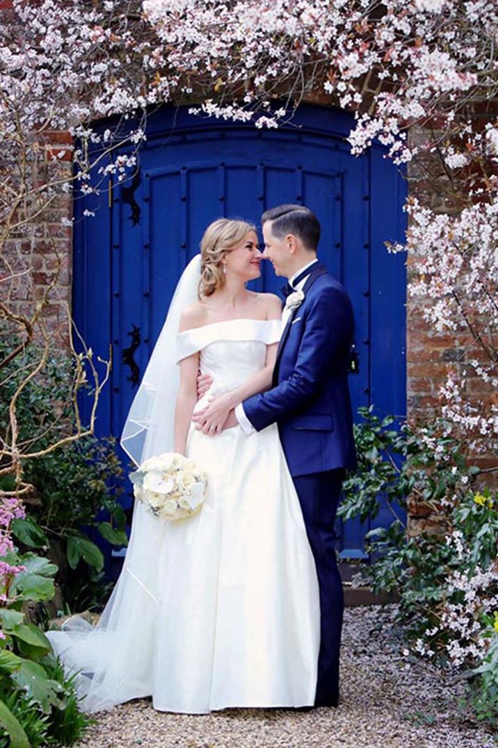 Bride in off the shoulder wedding dress with the groom in front of bright coloured door 