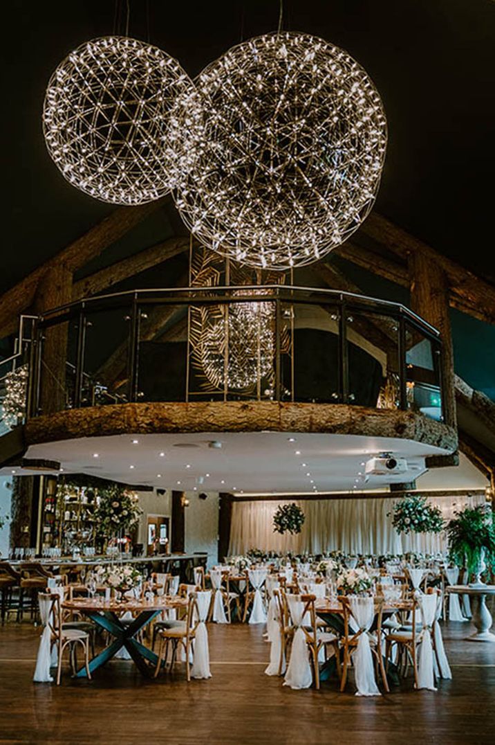 Cosy wedding tablescape with statement lighting installation with white fabric chair back decorations 