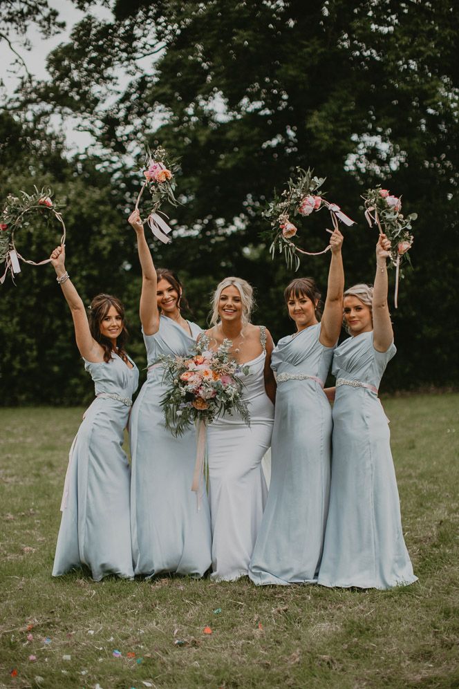 Bridesmaids in baby blue satin bridesmaid dresses holding their hoop bouquets in the air 