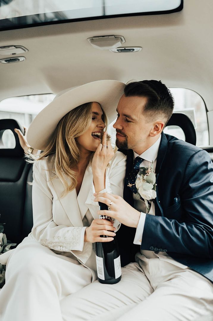 Bride in a vintage wedding suit and hat in the back on a London cab with her husband in a navy suit 