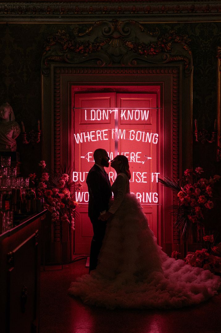 Pink neon sign with bride in tulle layered wedding dress standing with groom in front 