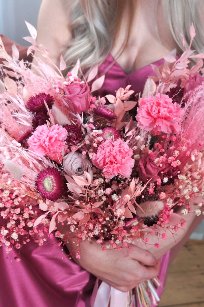 All pink preserved flower wedding bouquet with roses, gypsophila, bunny grass, and carnations held by bridesmaids in bright pink dress