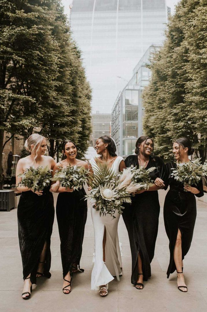 Bride in deep plunge neckline wedding dress walking with bridesmaids in mismatched black bridesmaid dresses 