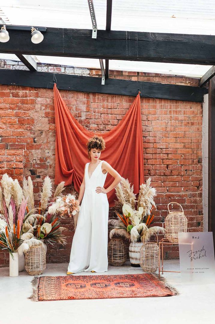 Bride in white bridal jumpsuit standing by large pampas grass wedding arrangements at The Shack Revolution - one of the most instagrammable wedding venues