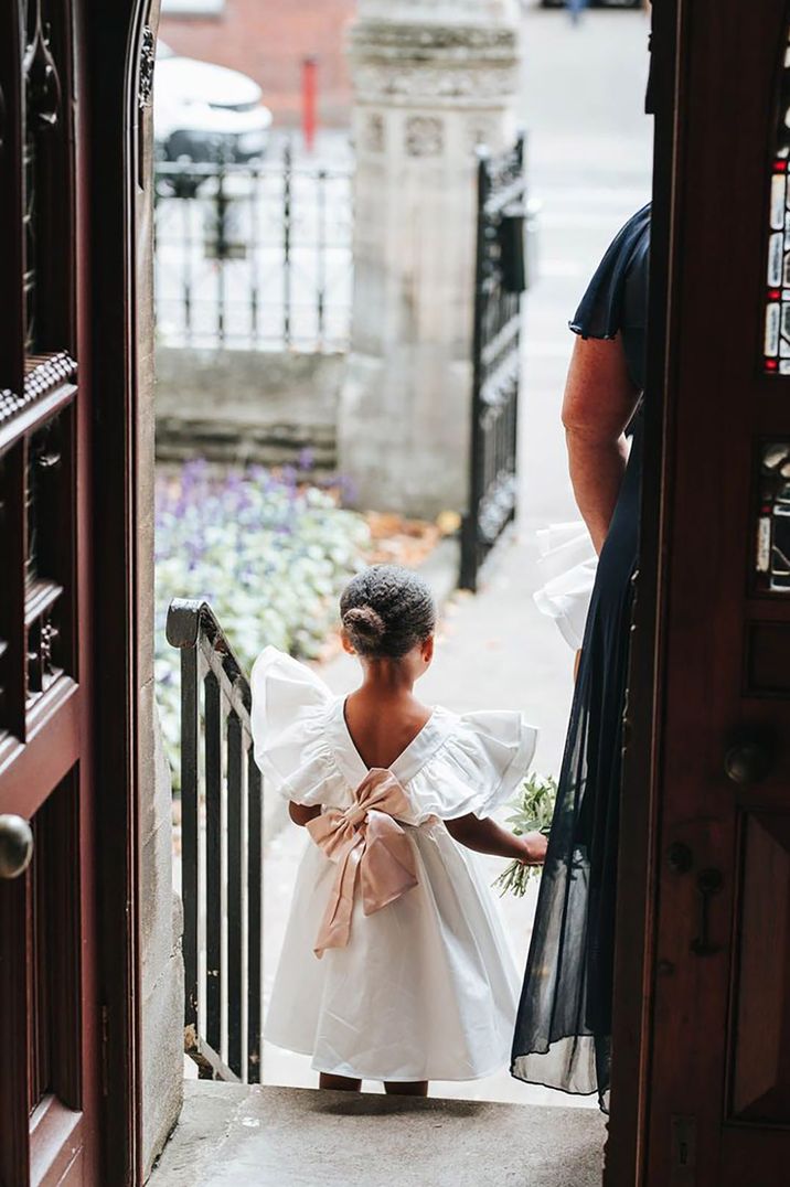 Young flower girl wearing a white dress with pink ribbon at registry office wedding