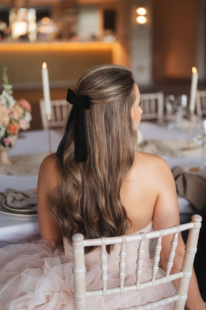 Bride with half up half down princess wedding hairstyle with black bow hair accessory