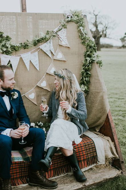 Couple on back of a truck with boho bunting and ivy floral garlands, bride in long lace wedding dress with wellies