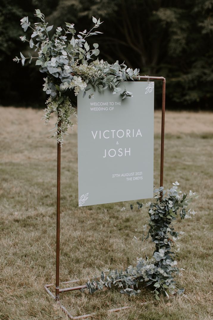 Pastel green and white welcome wedding sign on a copper frame with floral decor 