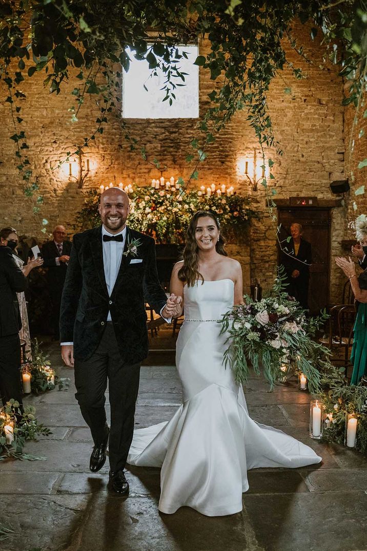 Bride and groom walking back down the aisle at Cripps Barn with fairy lights and candles