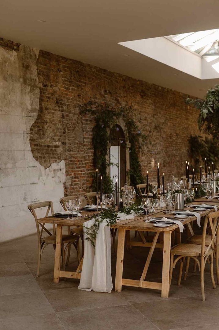 Neutral rustic wedding tablescape with white cloth table runners, foliage table runners and black tapered candles 