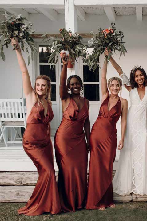 Bride wearing boho lace wedding dress standing with bridesmaids in burnt orange halterneck bridesmaid dresses 