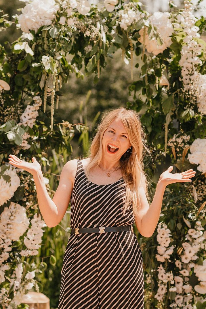 Wedding with white floral arch altar decoration with the wedding celebrant smiling in front of them