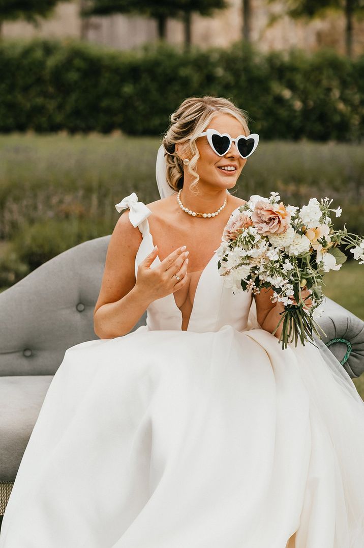 Bride in plunging wedding dress with retro sunglasses holding neutral wedding bouquet 