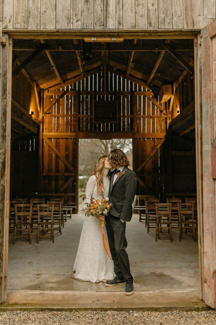 Bride in boho lace wedding dress posing with the groom at barn wedding 