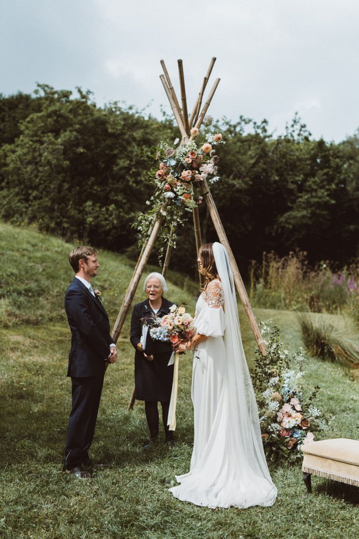 Bride and groom exchange vows at an outdoor ceremony with naked tipi altar and colourful wild flower decor 