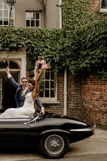 Bride in sleeveless wedding dress with cat eye sunglasses and groom in black convertible wedding car