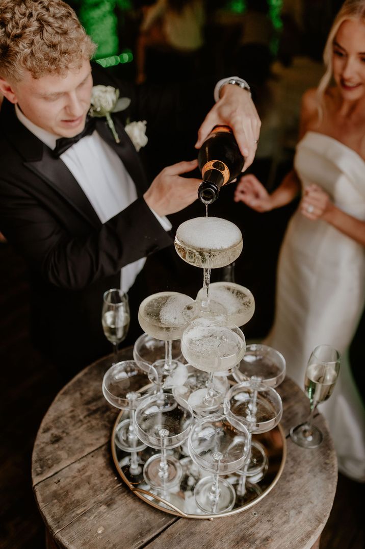 Bride in bandeau wedding dress and groom pouring champagne tower at wedding