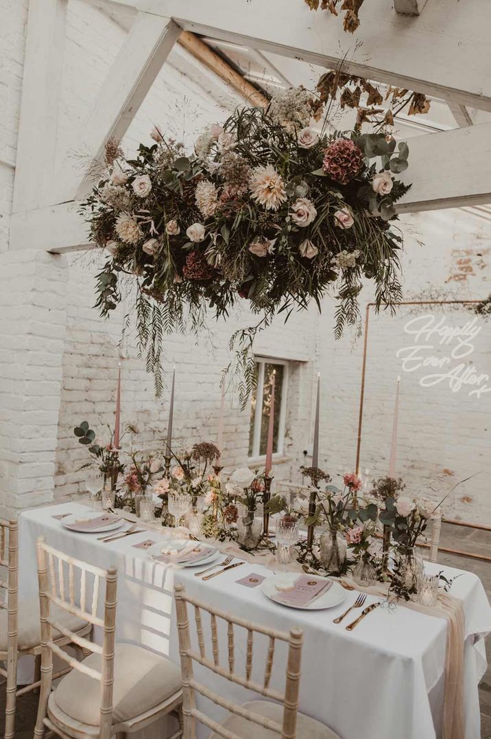 Suspended rose, peony and dried flower floral decor hanging over neutral wedding tablescape with tapered candles and dried flower arrangements at Garthmyl Hall Shropshire glasshouse wedding venue 