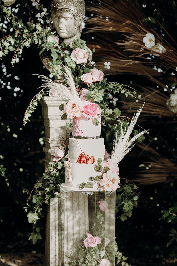 Three tier white iced wedding cake with two iced dogs and pampas grass decorations 