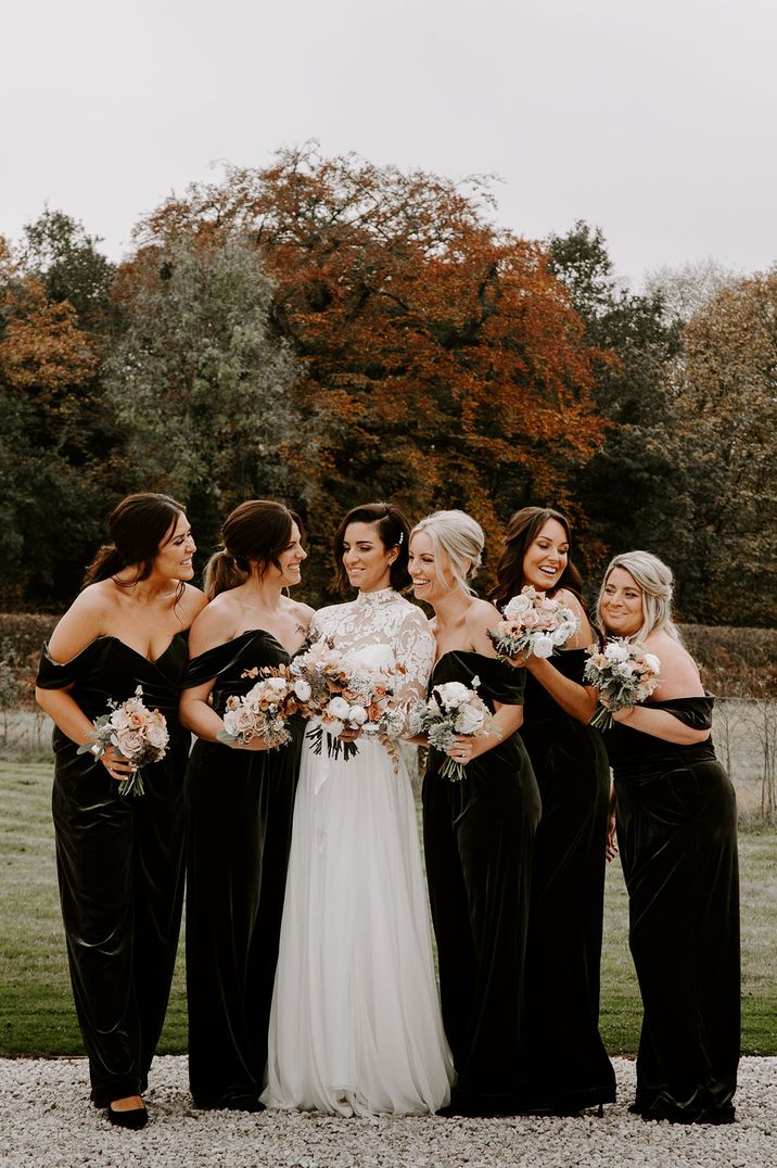 Bride in fitted lace wedding dress with long sleeves standing with bridesmaids in black bridesmaid dresses for winter wedding 