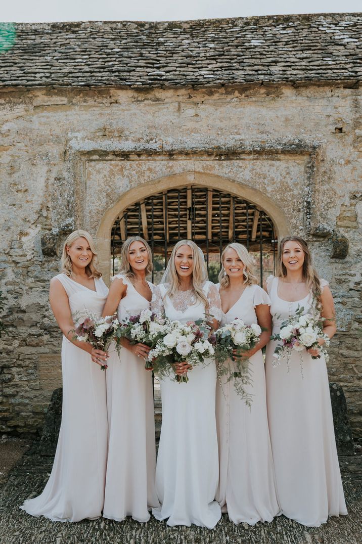 Blonde with with long wavy hair in a Charlie Brear wedding dress with lace caplet with her bridesmaids in white dresses 