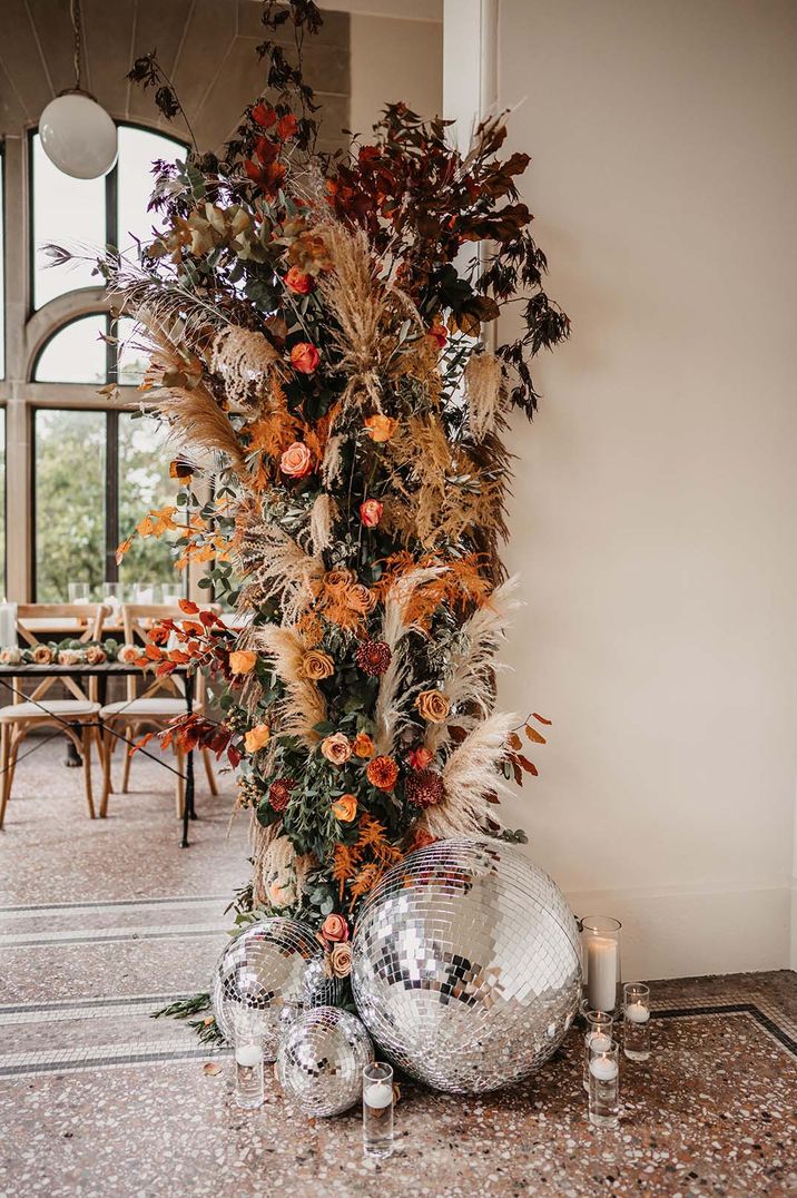 Flower column with orange and red flowers and coloured pampas grass with white pillar candles and disco balls 