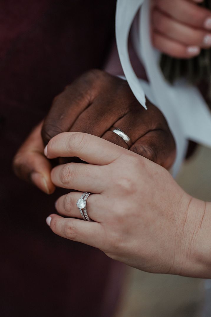 Bride and groom holding hands showing off their wedding rings and engagement ring 