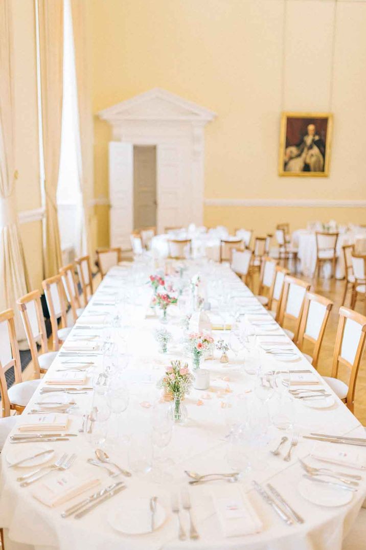 Classic wedding tablescape in dining hall of Farnham Castle with white tablecloth, delicate flower centrepieces and classic portraits on the wall 