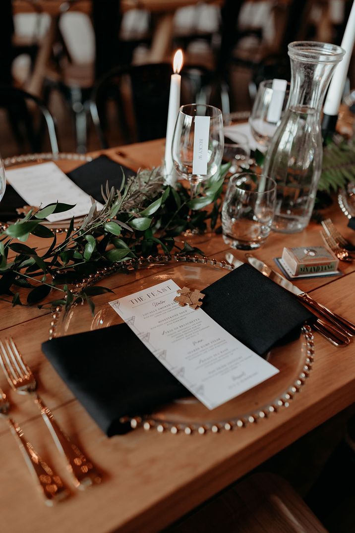 Christmas wedding place setting with gold charger plates with snowflake detail on black napkins and minimalist wedding menu 