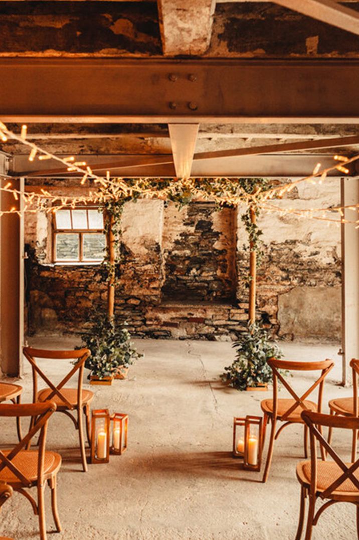 Wooden squared arch altar decoration with foliage, lanterns and fairy lights at barn wedding ceremony 