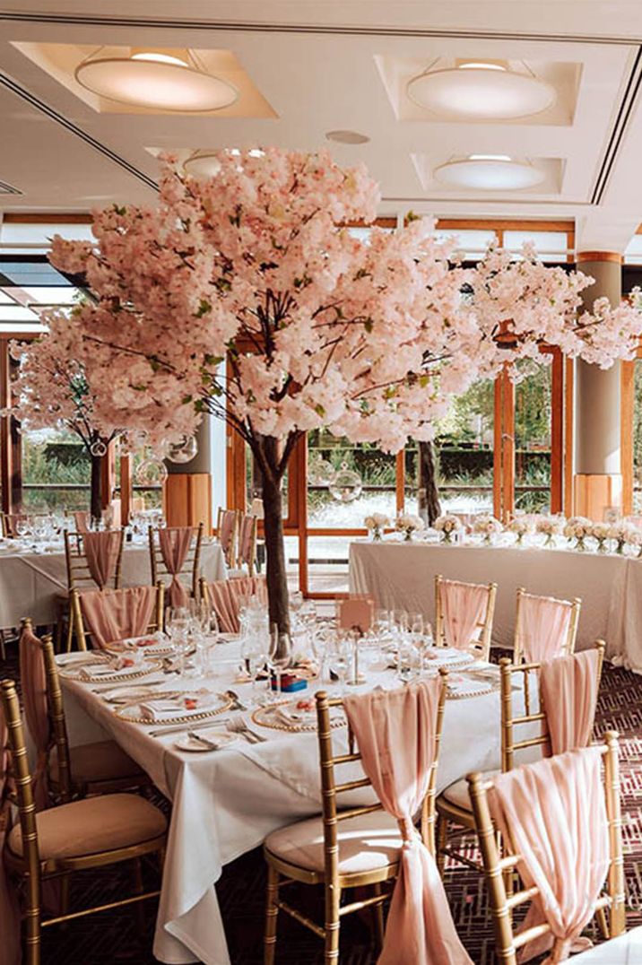 Square wedding tables at the wedding breakfast with pink table runner decorations and chair back decor with pink blossom tree table centrepiece