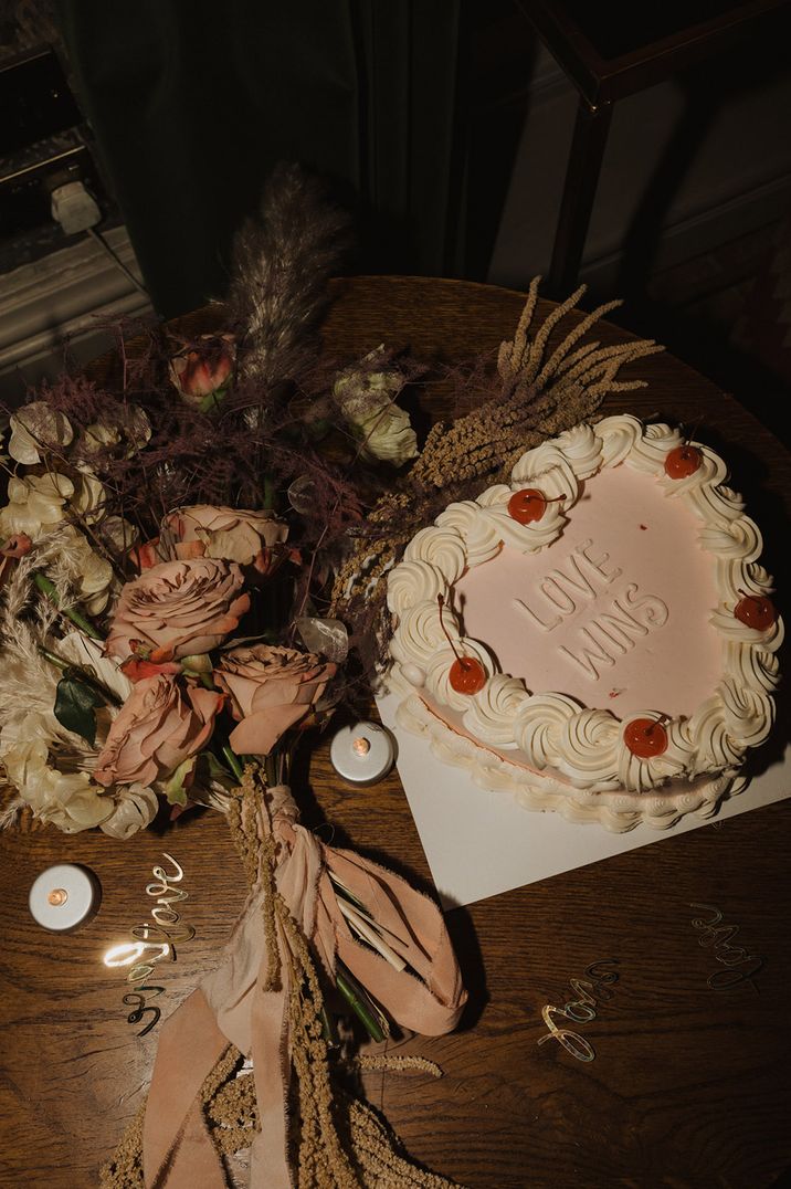 Heart shaped retro wedding cake with maraschino cherries with white icing spelling out 'Love Wins' 