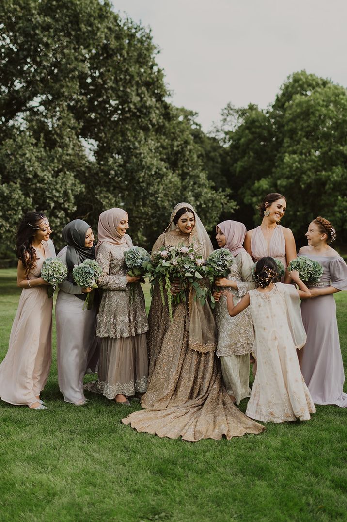 Bride in a gold wedding dress with her bridesmaids in metallic and pastel dresses standing by her side 