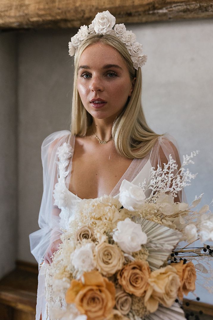 Bride holding beautiful neutral white and beige preserved wedding bouquet with roses and dried palm leaves 