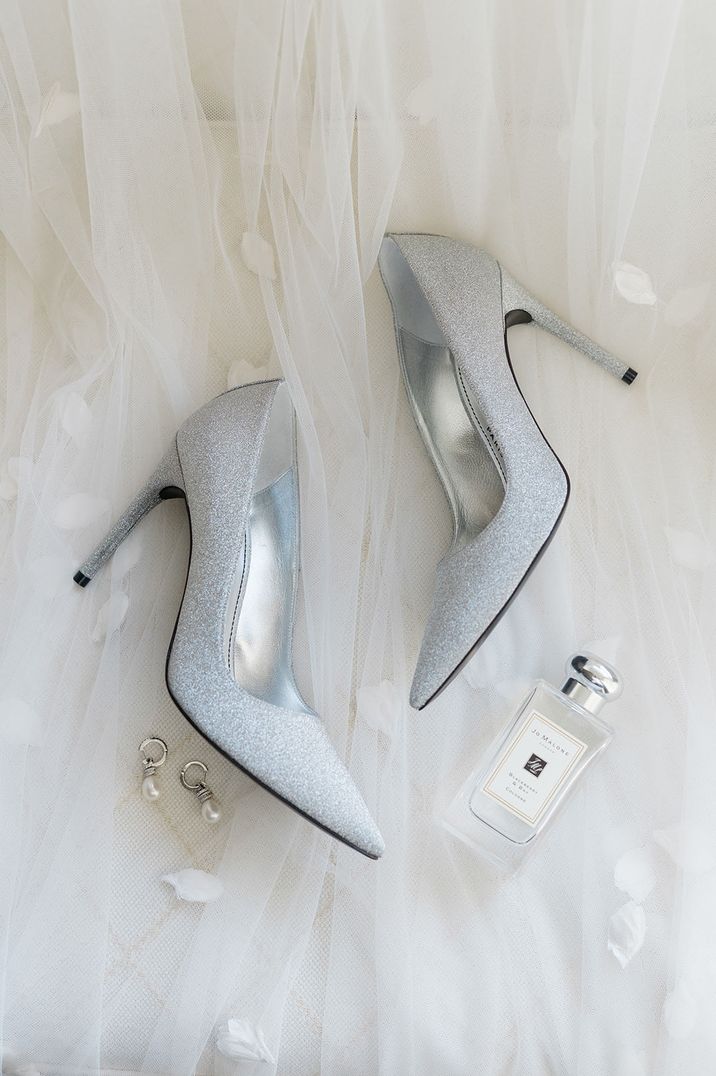 Pointed glittery wedding shoes with pearl earrings resting on top of the bride's wedding veil with Jo Malone London wedding scent 