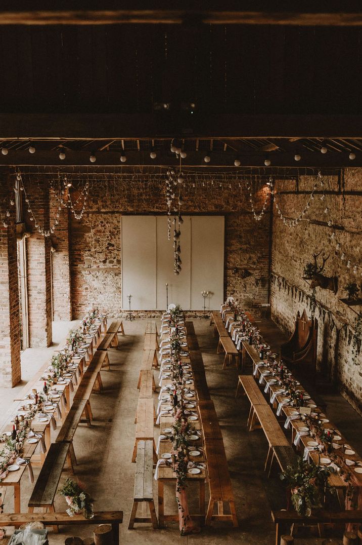 Medieval wedding venue with long banquet tables and benches with festoon lighting and greenery 