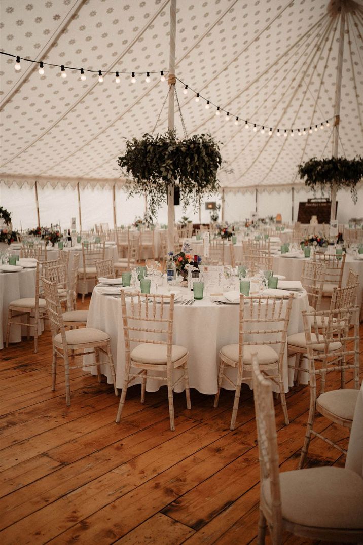 Marquee wedding with round tables decorated with white tablecloths and flowers with green coloured glassware 