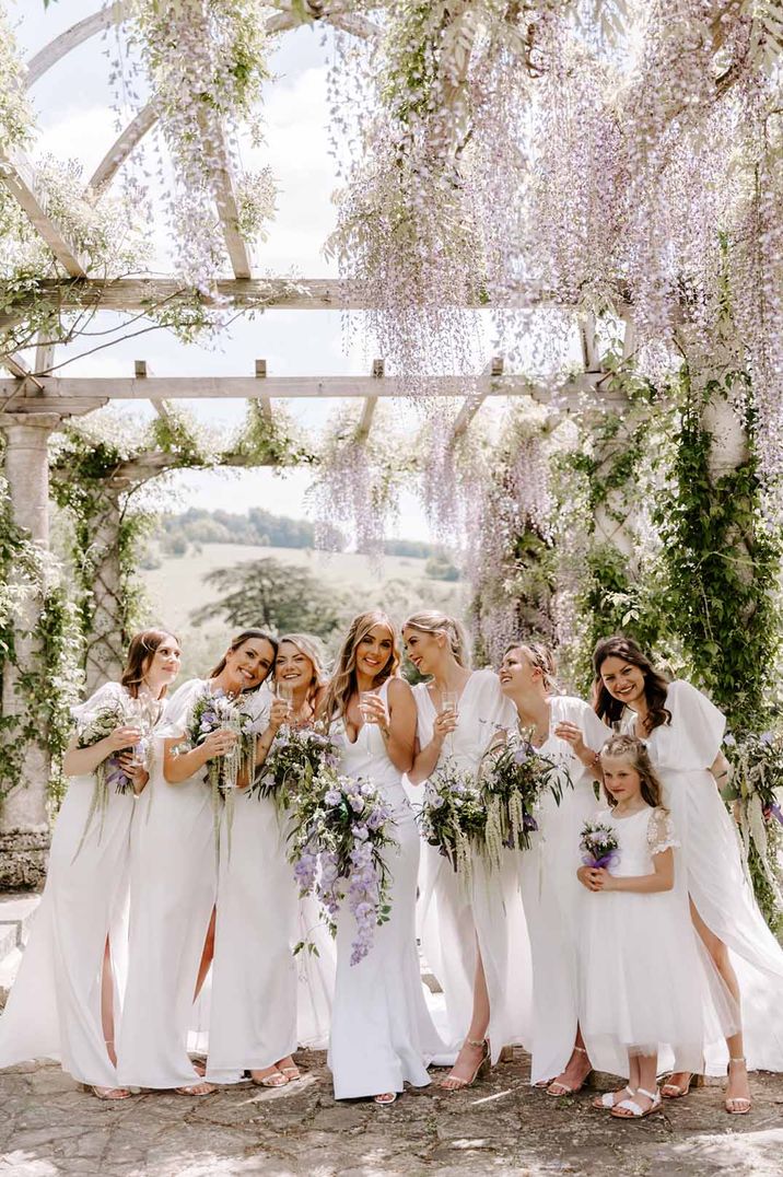 Bride in sleeveless wedding dress standing with bridal party all wearing mismatched white bridesmaid dresses 