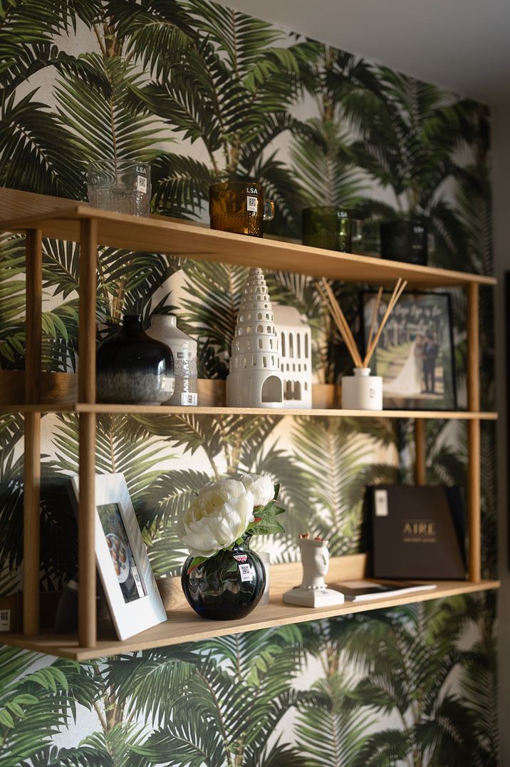 Palm tree wallpaper with wooden shelving, white vases and ornaments at The Wedding Shop 