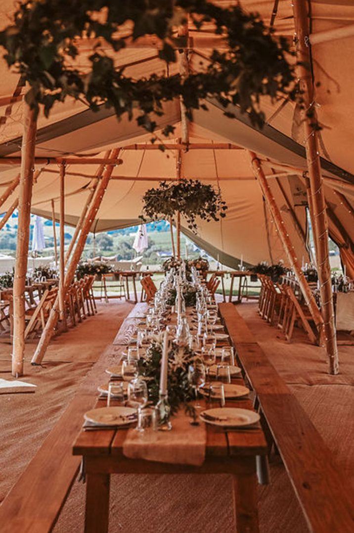 Tipi wedding with rustic wooden benches decorated with foliage and minimalist place settings 