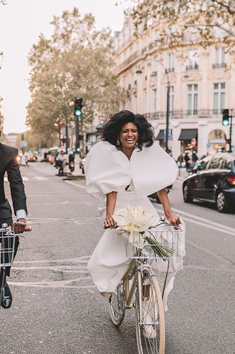 Couple on bicycles in Paris, bride in puff sleeve wedding dress and groom in black tux 